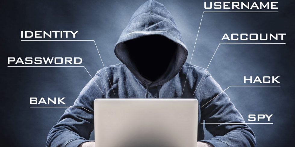 Ominous figure in a hoodie sitting at a laptop.