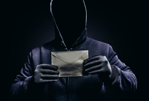 Photo of scary hooded man holding letter.