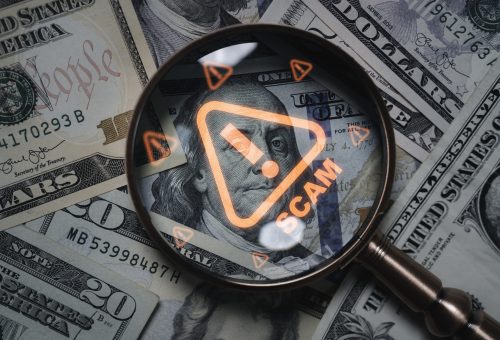 Magnifying glass focusing on scam warning symbol over dollar bills concept of financial fraud money laundering cybercrime and online scam alert for security awareness and finance protection