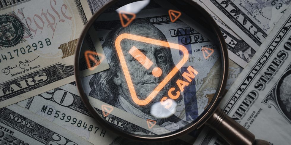 Magnifying glass focusing on scam warning symbol over dollar bills concept of financial fraud money laundering cybercrime and online scam alert for security awareness and finance protection